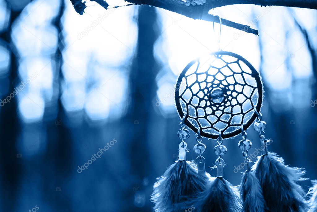 Dreamcatcher made of feathers, leather, beads, and ropes in classic blue trendy color of the year 2020.