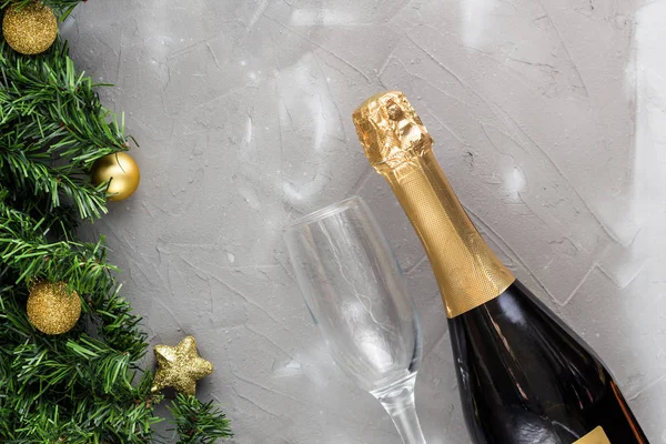 Two champagne glasses with gold balls and golden champagne bottle, green fir tree on grey background, copy space.