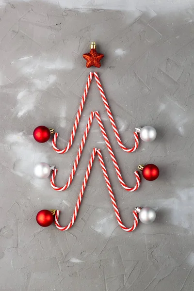 Godis käppar i form av julgran med stjärna och boll på grå bakgrund. Semesterabstrakt begrepp. — Stockfoto