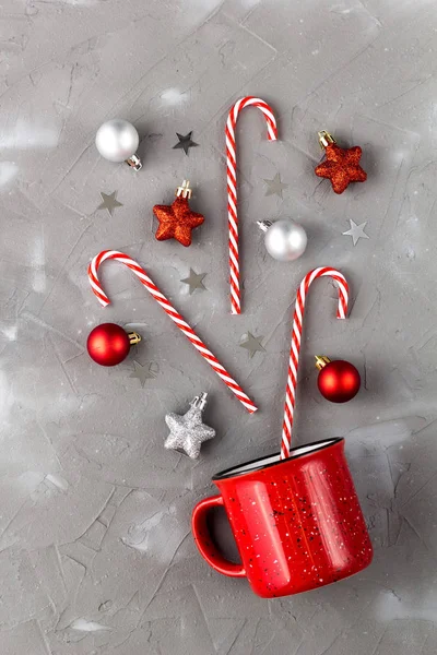 Czerwony kubek z trzciny cukrowej, piłkę i gwiazdy na szarym tle. Koncepcja Bożego Narodzenia i Nowego Roku. — Zdjęcie stockowe