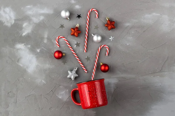 Röd kopp med godis käpp, boll och stjärnor på grå bakgrund. Jul- och nyårskoncept. — Stockfoto