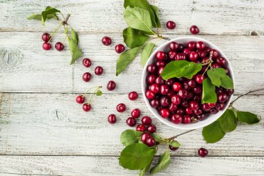 Taze kirazlar, beyaz kase ve ahşap zeminde su damlaları.