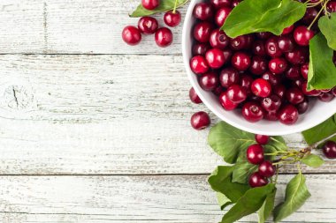 Taze kirazlar, beyaz kase ve ahşap zeminde su damlaları.