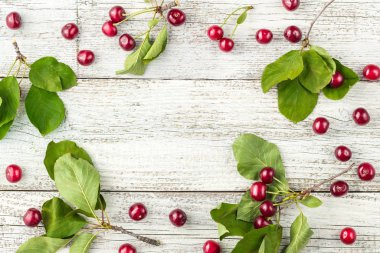 Beyaz ahşap zemin üzerinde kırmızı kiraz çileği ve yeşil yapraklar çerçevesi. en üstteki görünüm