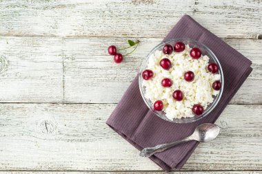 Beyaz ahşap arka planda şeffaf kasede kirazlı süzme peynirden kahvaltı.
