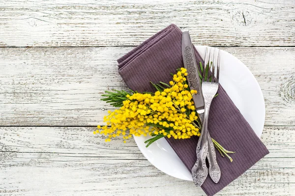 Святкова тарілка столу з серветкою виделкою та ножем та прикрасою квітів мімози на білому дерев'яному фоні — стокове фото