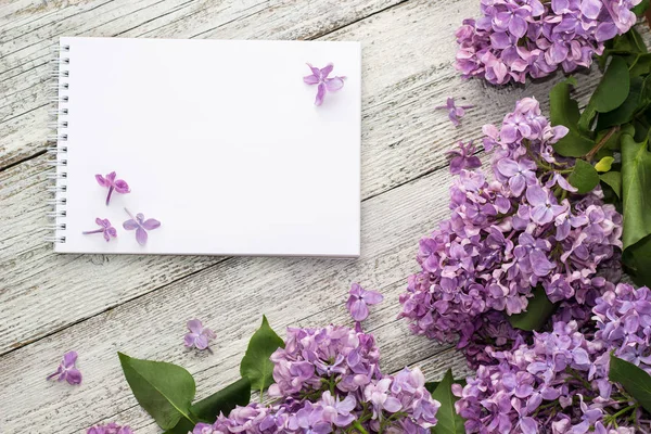 Clean notepad with spring lilac flowers on white wooden background