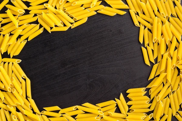 Rahmen eines Haufens Penne Pasta auf schwarzem Hintergrund mit Copyspace — Stockfoto