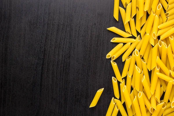 Rand eines Haufens Penne Pasta auf schwarzem Hintergrund mit Kopierraum — Stockfoto