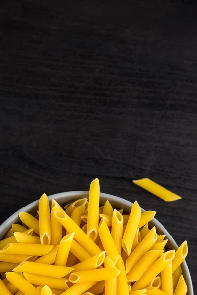 Vista superior de fondo negro con penne crudo italiano o pasta en tazón con espacio para copiar — Foto de Stock