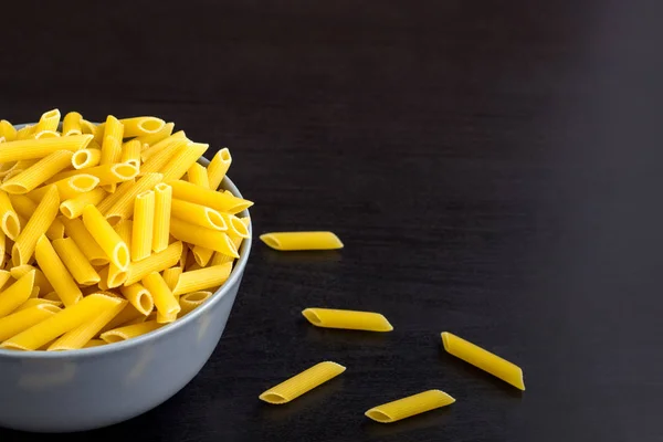 Black background with italian raw penne or pasta in bowl with copy space — Stock Photo, Image