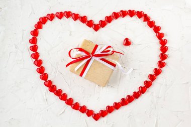 Sevgililer Günü için beyaz masadaki kalplerin kalbine kırmızı ve beyaz kurdele takılmış hediye kutusu..