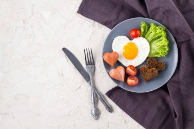 Gri tabakta servis edilen kalp şeklinde sahanda yumurtalarla Sevgililer Günü kahvaltısı.