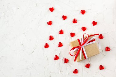 Sevgililer Günü için kırmızı ve beyaz kurdeleli hediye kutusu ve beyaz masada kalpler.