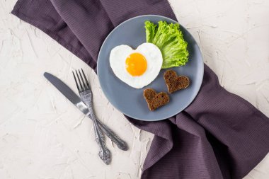 Gri tabakta servis edilen kalp şeklinde sahanda yumurtalarla Sevgililer Günü kahvaltısı