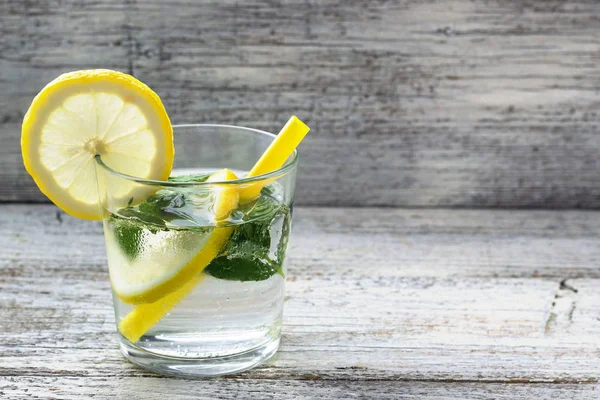 Agua con limón y menta en un vaso sobre fondo de madera. Bebida fresca de limonada de verano — Foto de Stock