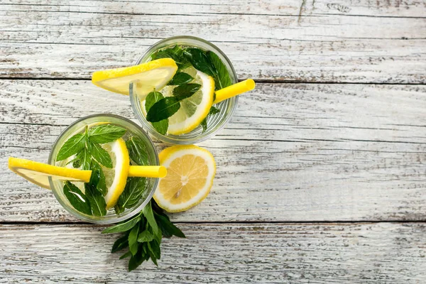 Dos vasos de limonada con limón, menta y cubitos de hielo sobre fondo de madera. Bebida de verano — Foto de Stock
