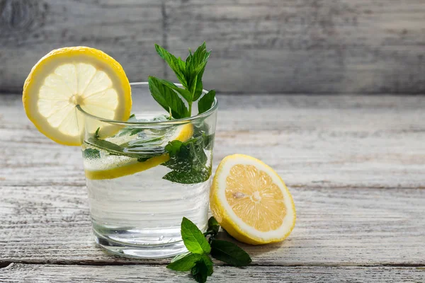 Agua con limón y menta en un vaso sobre fondo de madera. Bebida fresca de limonada de verano — Foto de Stock