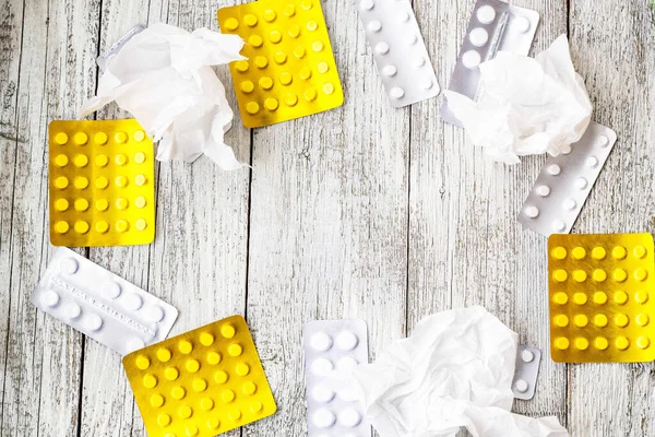 Frame of tablets in blister packs and pills and handkerchiefs on white wooden background. Medicines concept with copy space