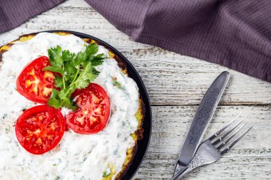 Domatesli kabak keki ve beyaz ahşap arka planda taze maydanoz. Peçete çatalı ve bıçakla üst manzara