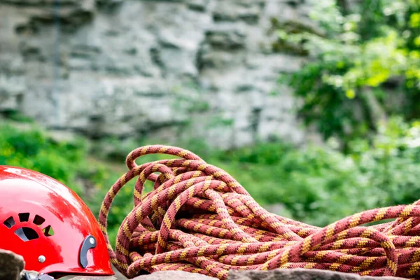 Rope access tools: hard hat, rope, carabiner. Mountaineering equipment on rocks against a background of rocks and greenery
