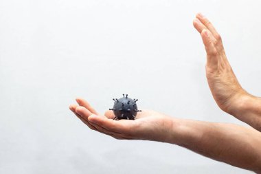 İnsan eli, gri bir koronavirüs molekülünün bir kopyasını tutar. Beyaz arka planda covid-19 korunması kavramı