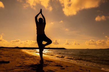 Sahilde gün batımında siluet kadın yogası. Spor ve sağlıklı yaşam tarzı. Güne yeni bir başlangıç ve dinlenme.