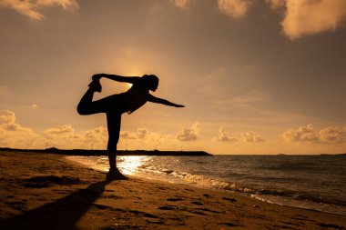 Sahilde gün batımında siluet kadın yogası. Spor ve sağlıklı yaşam tarzı. Güne yeni bir başlangıç ve dinlenme.
