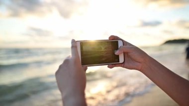 Taylandlı kadın cep telefonuyla fotoğraf çekiyor. Asyalı kadın yaz plajında yalnız seyahat ediyor.