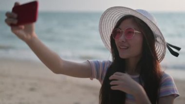 Genç Taylandlı kadın cep telefonuyla fotoğraf çekiyor. Asyalı kadın yaz plajında yalnız seyahat ediyor.