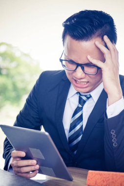 Asyalı İşadamı tablet üzerinde çalışıyor, çalışmak için baskı görüyor ve başarısız oluyor