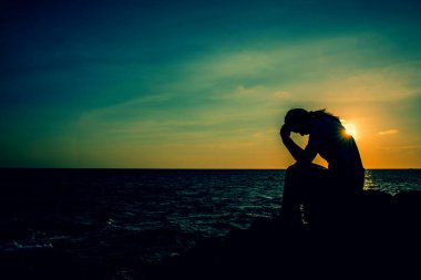 Siluet kadın kayanın üzerinde tek başına oturuyor. Üzgün ve yalnız..