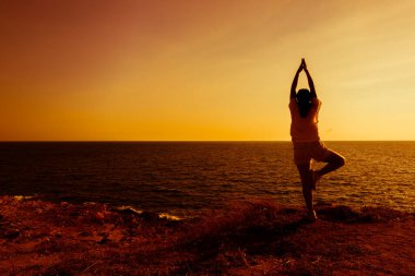 Gün batımında dağda yoga yapan bir kadın silueti. Spor ve sağlıklı yaşam tarzı