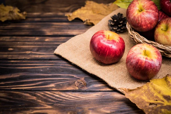 木のテーブルの上に落ちたカエデの葉を背景に熟した新鮮なリンゴのクローズアップショット — ストック写真