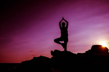 Gün batımında dağda yoga yapan bir kadın silueti. Spor ve sağlıklı yaşam tarzı