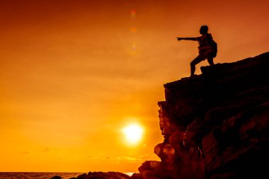 Gün batımında uçurumda bir kadın silueti, başarı konsepti.