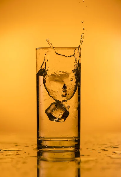 Stänk av fallande is i ett glas med vatten — Stockfoto