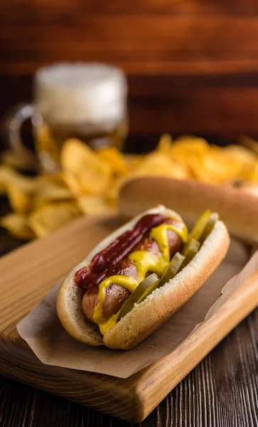Hot dog on a background of chips and beer on a wooden board