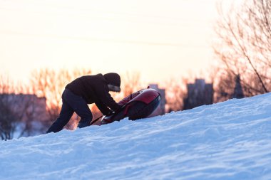 Bir çocuk gün batımında karlı bir dağa boru çekiyor