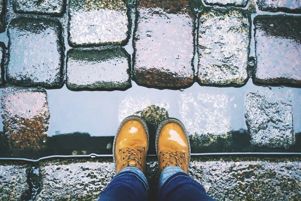 Yağmur sonrası sarı Ayakkabı ve kot ıslak bir eski kaldırım taşı arka plan üzerinde ayaklarda bakın.