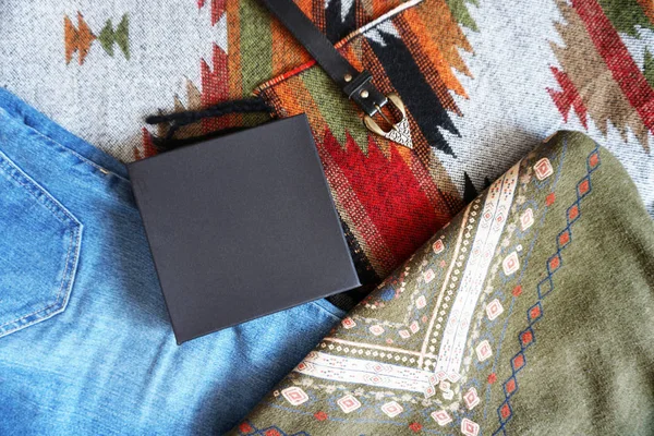 Black paper box on the background of patterned fabrics in boho style. Top view.