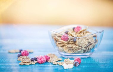 Bir kase mısır gevreği ve mavi ahşap arka planda yabanmersini.