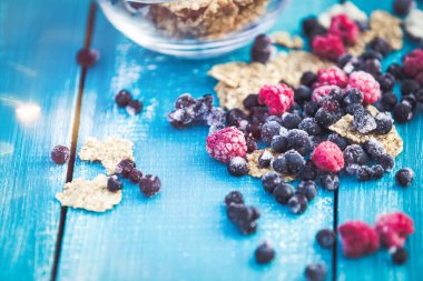 Bir kase mısır gevreği ve mavi ahşap arka planda yabanmersini.