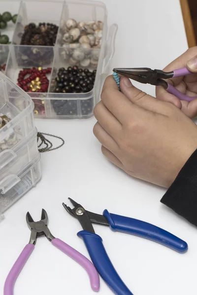 Person making jewelry with beads and other materials with tools
