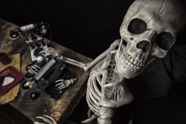 Halloween Skeleton At a Table with Typewriter, Phone and Cookies clipart