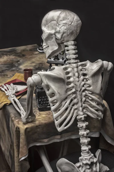 Esqueleto de Halloween en una mesa con máquina de escribir, teléfono y cookies —  Fotos de Stock