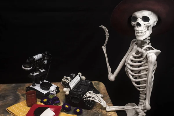 Esqueleto de Halloween en una mesa con máquina de escribir, teléfono y cookies — Foto de Stock