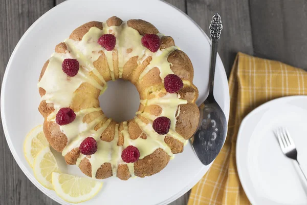 Citrón koláč ojíněný s žlutým cukrové polevy a červených malin — Stock fotografie