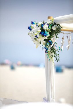 Açık hava düğün balosu çardağı kumsalda mavi ve beyaz çiçeklerle süslenmiş ve deniz yıldızıyla süslenmiş.