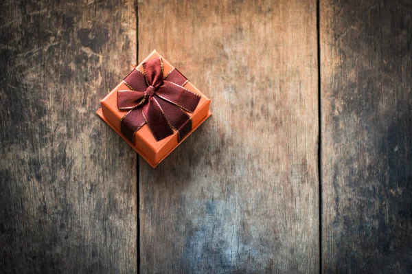 Boîte cadeau de couleur orange attachée avec arc écarlate sur fond en bois — Photo